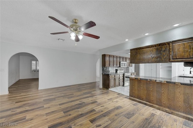 kitchen featuring ceiling fan, decorative backsplash, a textured ceiling, wood-type flooring, and stainless steel appliances