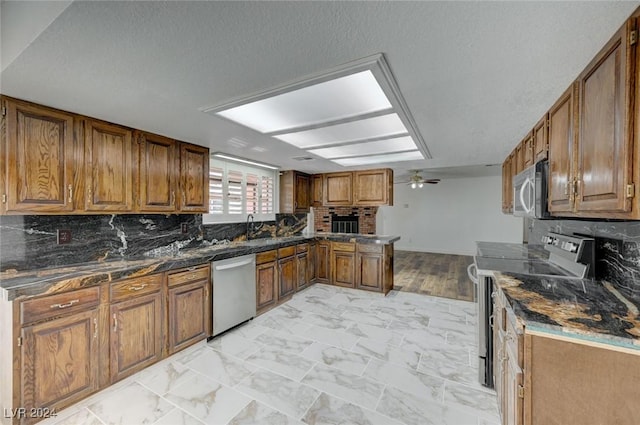 kitchen featuring kitchen peninsula, appliances with stainless steel finishes, backsplash, ceiling fan, and dark stone countertops