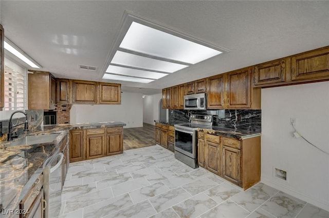 kitchen with tasteful backsplash, sink, dark stone counters, and stainless steel appliances