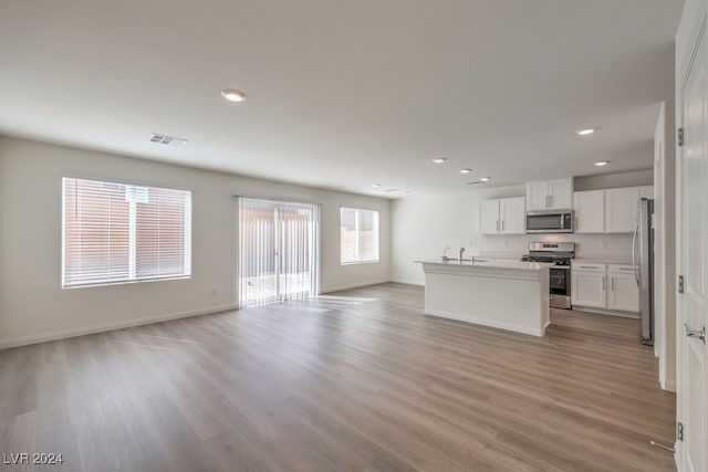 kitchen featuring white cabinets, appliances with stainless steel finishes, light hardwood / wood-style floors, and an island with sink