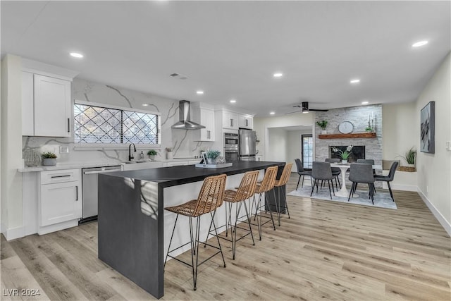 kitchen with white cabinetry, light wood-type flooring, wall chimney range hood, and appliances with stainless steel finishes