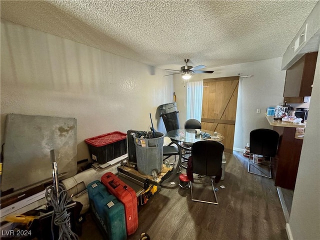 home office featuring a barn door, ceiling fan, dark wood-type flooring, and a textured ceiling