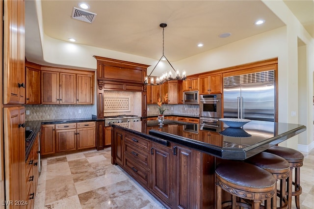 kitchen featuring a chandelier, built in appliances, backsplash, and an island with sink