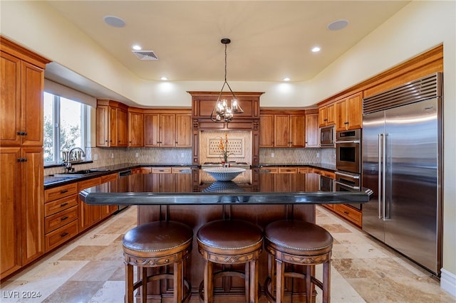 kitchen with sink, a notable chandelier, built in appliances, pendant lighting, and a kitchen island