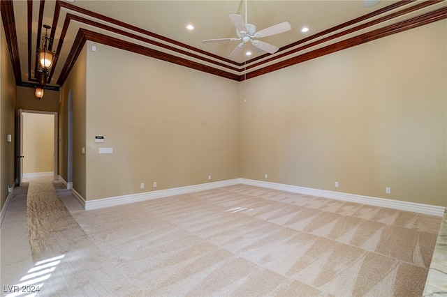 empty room featuring ceiling fan, crown molding, a high ceiling, and light carpet