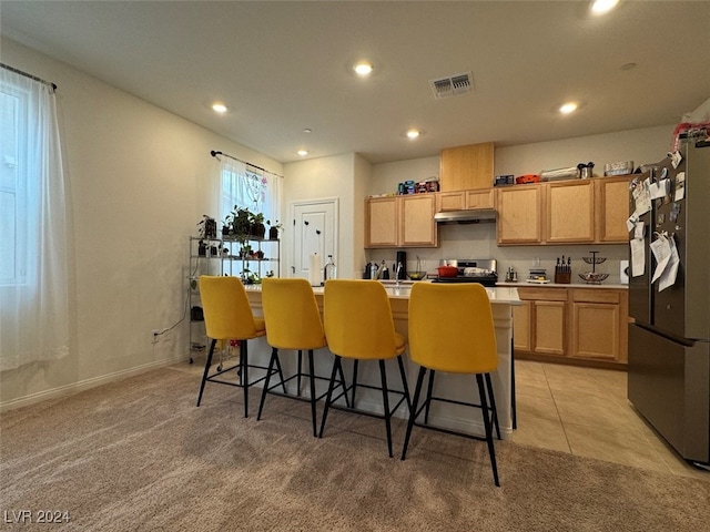 kitchen with light carpet, black refrigerator, a center island with sink, and light brown cabinets