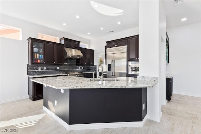 kitchen featuring backsplash, sink, light stone countertops, appliances with stainless steel finishes, and a large island