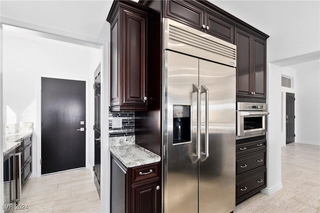 kitchen with backsplash, dark brown cabinetry, light stone countertops, and appliances with stainless steel finishes