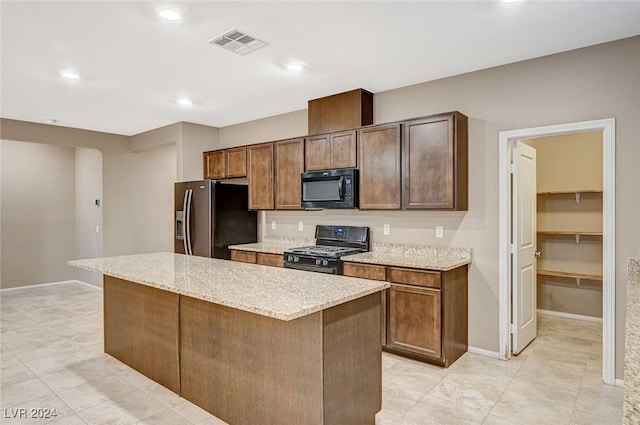 kitchen with light stone countertops, light tile patterned floors, a kitchen island, and black appliances