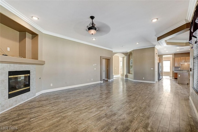 unfurnished living room with a tiled fireplace, ceiling fan, hardwood / wood-style floors, and ornamental molding