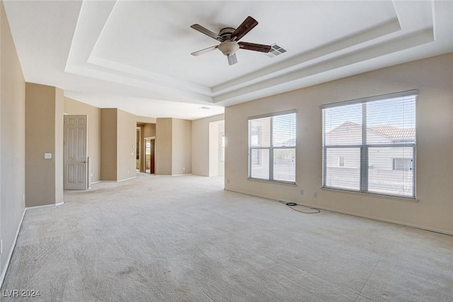 unfurnished living room with a tray ceiling, ceiling fan, and light colored carpet