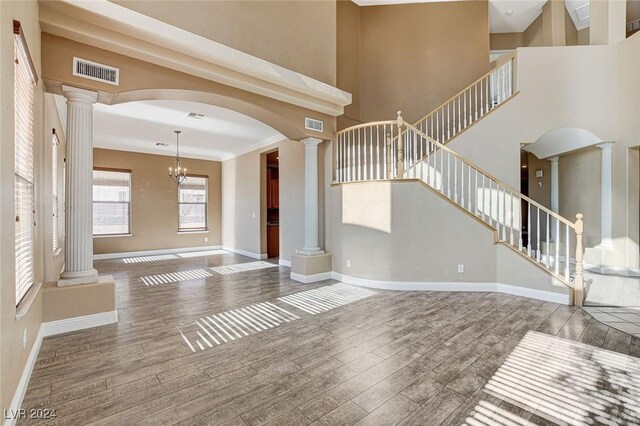 foyer featuring wood-type flooring, a towering ceiling, decorative columns, and a notable chandelier