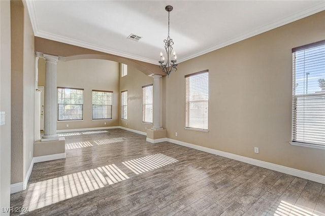 unfurnished room featuring wood-type flooring, decorative columns, an inviting chandelier, and crown molding