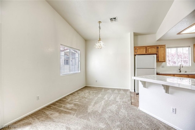 kitchen with light carpet, decorative light fixtures, white fridge, tile counters, and lofted ceiling