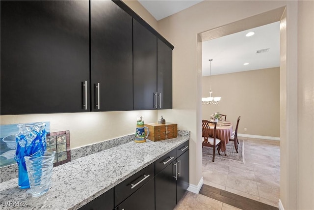 kitchen with a notable chandelier, light tile patterned flooring, light stone countertops, and decorative light fixtures