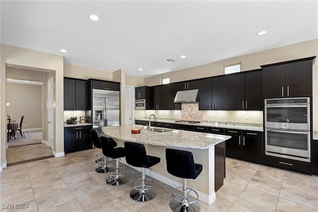 kitchen with light stone countertops, sink, a kitchen breakfast bar, an island with sink, and appliances with stainless steel finishes