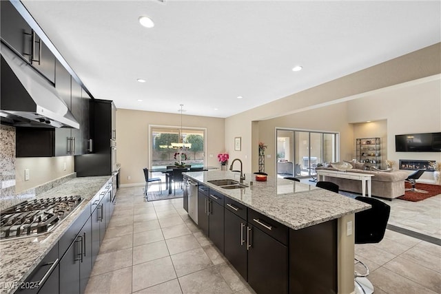 kitchen featuring appliances with stainless steel finishes, sink, light tile patterned floors, decorative light fixtures, and a center island with sink