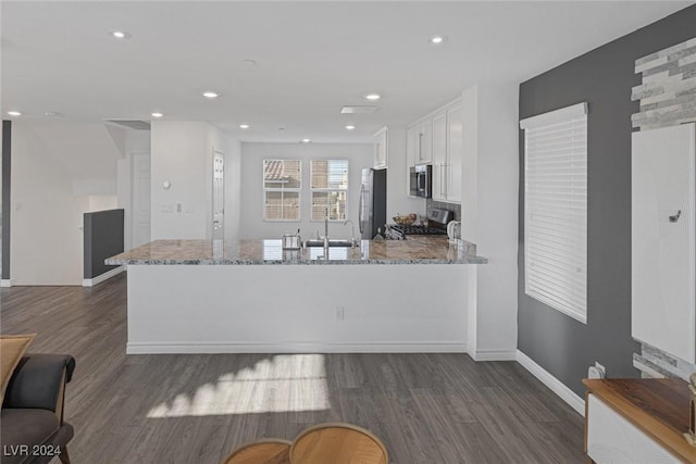 kitchen featuring light stone countertops, stainless steel appliances, dark hardwood / wood-style flooring, kitchen peninsula, and white cabinets