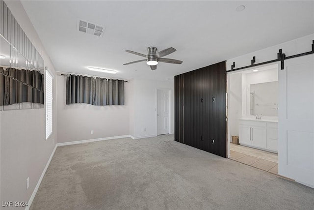 unfurnished bedroom featuring ensuite bath, light colored carpet, ceiling fan, sink, and a barn door