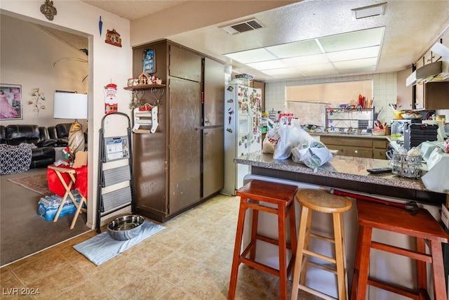 kitchen with kitchen peninsula, dark brown cabinets, a breakfast bar, and white fridge with ice dispenser