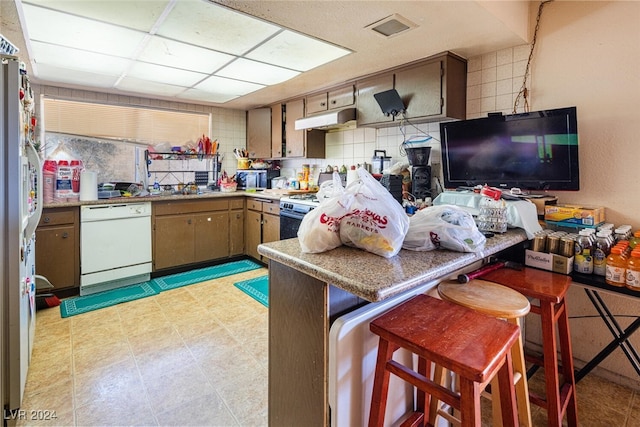 kitchen featuring white appliances, sink, decorative backsplash, a kitchen bar, and kitchen peninsula