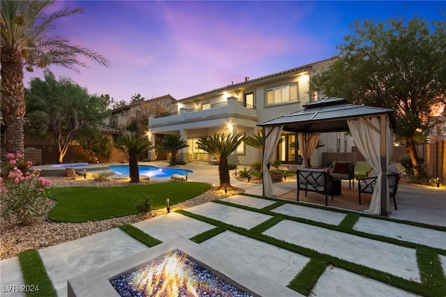 back house at dusk featuring a gazebo, a patio area, a balcony, and an outdoor living space with a fire pit