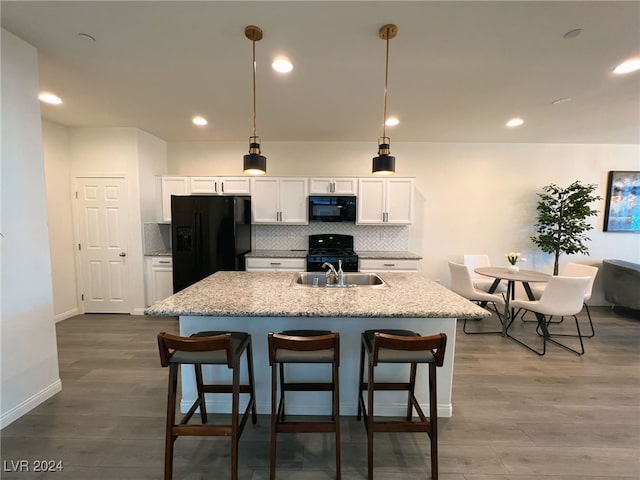 kitchen featuring light stone countertops, black appliances, hardwood / wood-style floors, white cabinetry, and hanging light fixtures