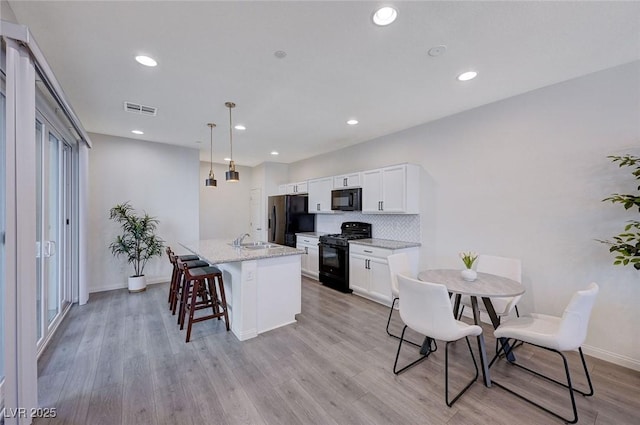 kitchen with white cabinets, hanging light fixtures, black appliances, light stone countertops, and a center island with sink