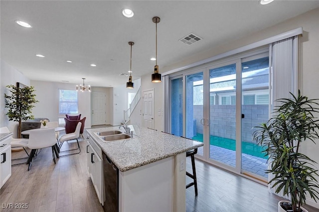 kitchen featuring pendant lighting, white cabinetry, black dishwasher, sink, and a center island with sink