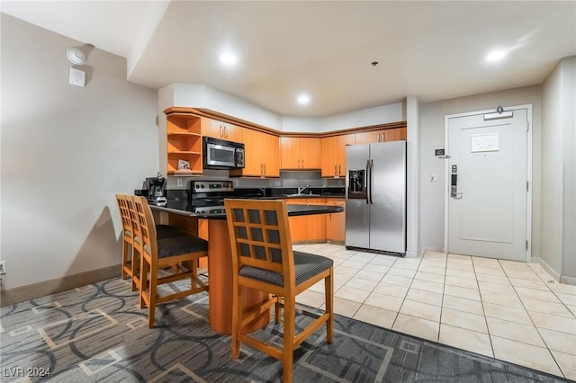 kitchen featuring a breakfast bar area, kitchen peninsula, light tile patterned floors, and appliances with stainless steel finishes