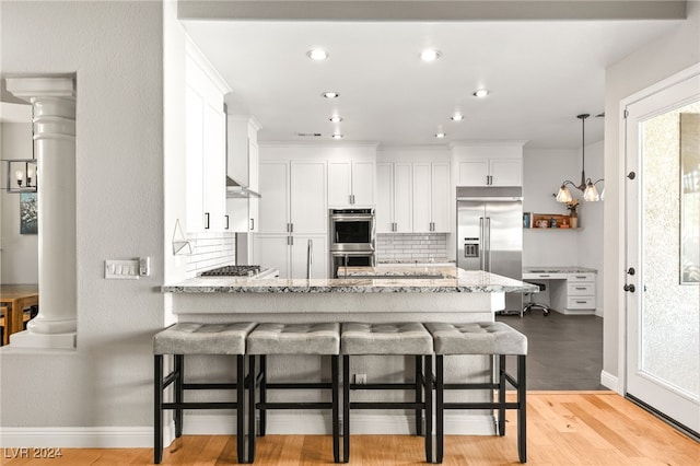 kitchen with white cabinets, light hardwood / wood-style flooring, light stone counters, kitchen peninsula, and stainless steel appliances