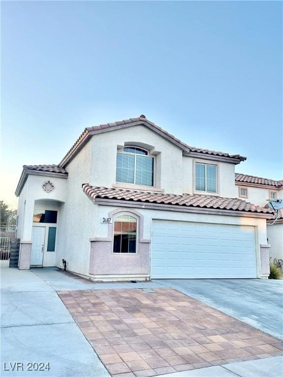 view of front facade with stucco siding, a tiled roof, concrete driveway, and a garage