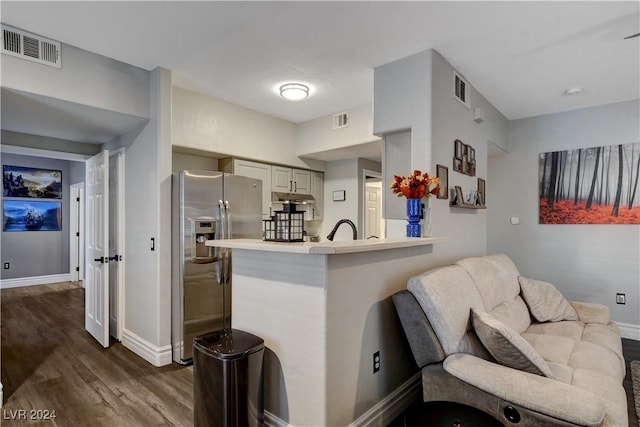 kitchen featuring sink, dark hardwood / wood-style flooring, stainless steel refrigerator with ice dispenser, kitchen peninsula, and a kitchen bar