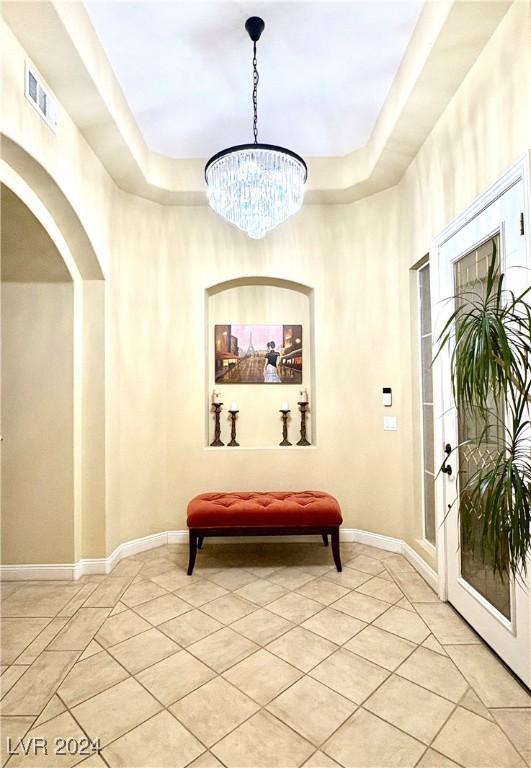 entryway with light tile patterned floors, baseboards, visible vents, a tray ceiling, and a notable chandelier