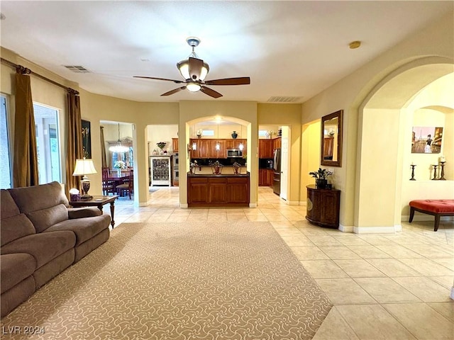 living area featuring arched walkways, light tile patterned floors, visible vents, a ceiling fan, and baseboards