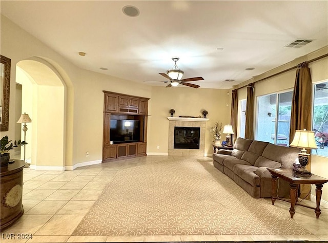 living area with light tile patterned floors, visible vents, arched walkways, a ceiling fan, and a tile fireplace