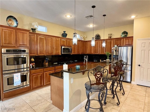 kitchen with decorative light fixtures, stainless steel appliances, visible vents, brown cabinetry, and an island with sink