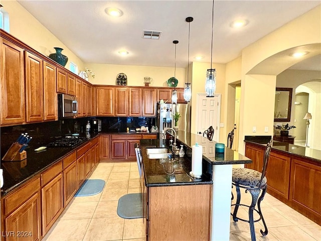 kitchen with tasteful backsplash, stainless steel appliances, a kitchen island with sink, sink, and decorative light fixtures