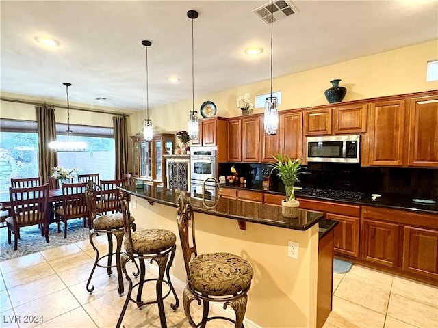 kitchen with appliances with stainless steel finishes, a kitchen island with sink, light tile patterned floors, pendant lighting, and a breakfast bar area