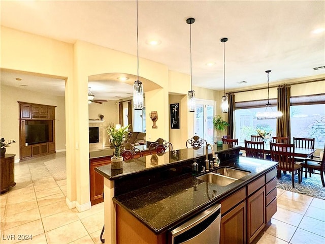 kitchen featuring a center island with sink, stainless steel dishwasher, a fireplace, a sink, and light tile patterned flooring