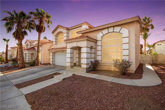 mediterranean / spanish house featuring an attached garage, stucco siding, driveway, and fence