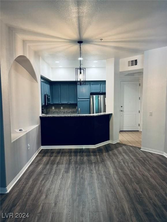 kitchen with pendant lighting, dark wood-type flooring, blue cabinets, stainless steel fridge, and kitchen peninsula