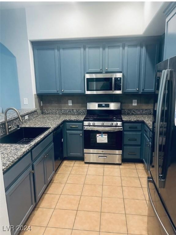 kitchen with light stone counters, stainless steel appliances, sink, blue cabinetry, and light tile patterned flooring