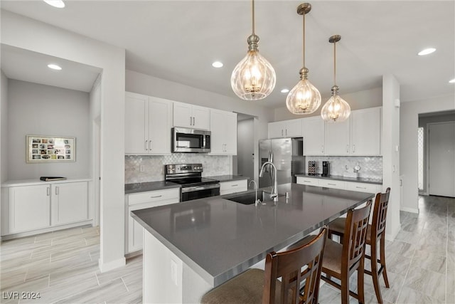 kitchen with stainless steel appliances, sink, pendant lighting, white cabinetry, and an island with sink