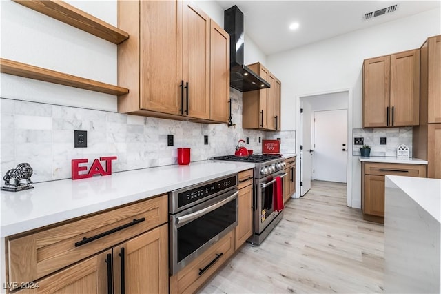 kitchen with wall chimney exhaust hood, light hardwood / wood-style floors, decorative backsplash, and stainless steel appliances