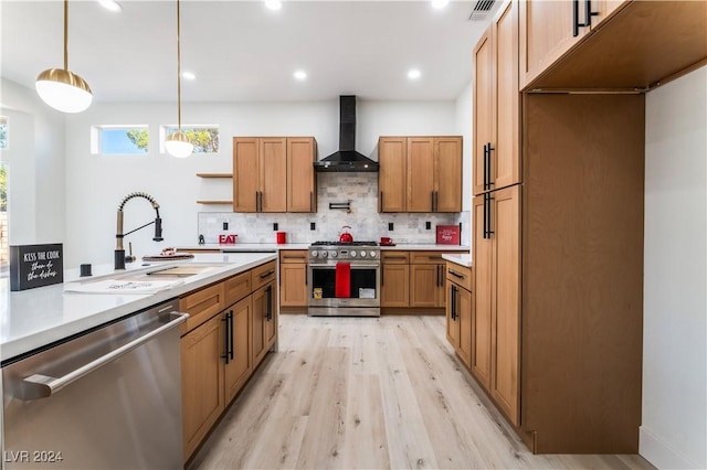 kitchen with sink, wall chimney exhaust hood, light hardwood / wood-style flooring, pendant lighting, and appliances with stainless steel finishes