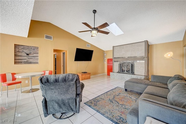 living room featuring lofted ceiling with skylight, ceiling fan, a textured ceiling, a fireplace, and light tile patterned flooring