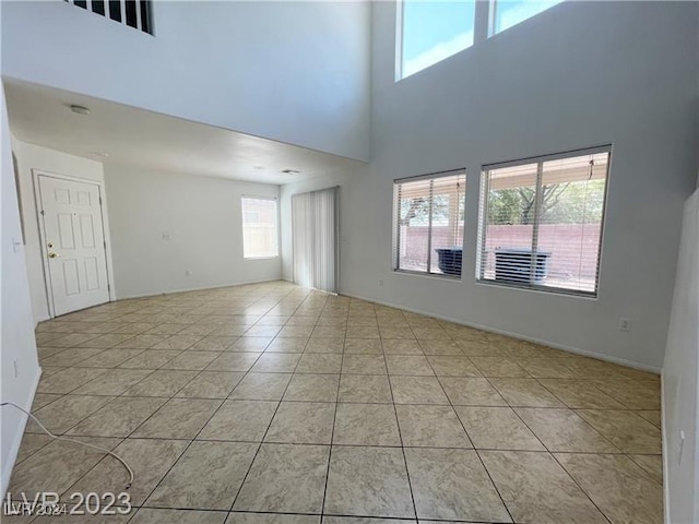 tiled empty room featuring a towering ceiling and a wealth of natural light