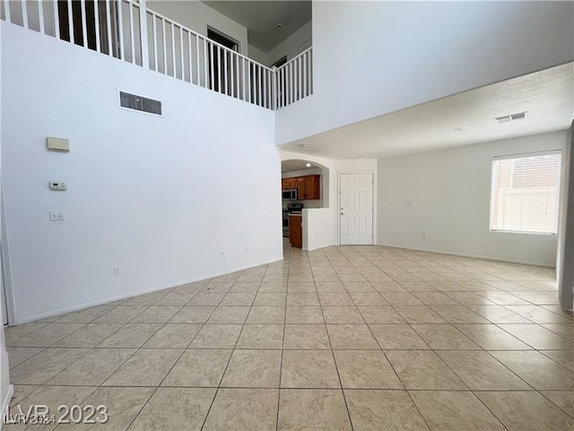 unfurnished living room featuring light tile patterned flooring and a towering ceiling