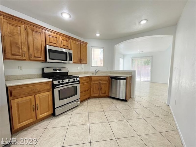 kitchen with kitchen peninsula, appliances with stainless steel finishes, sink, and light tile patterned flooring